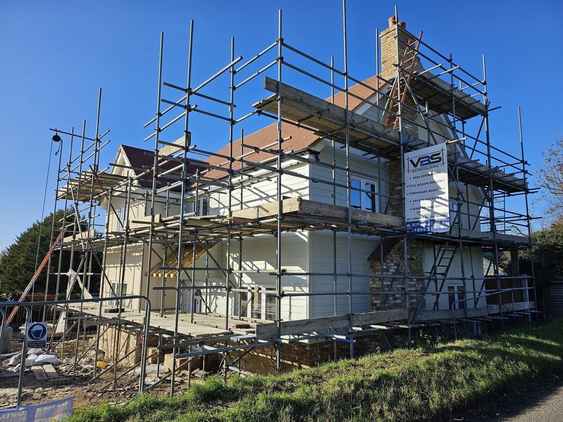 House under renovation with scaffolding, pale exterior, brown roof, and clear blue sky.