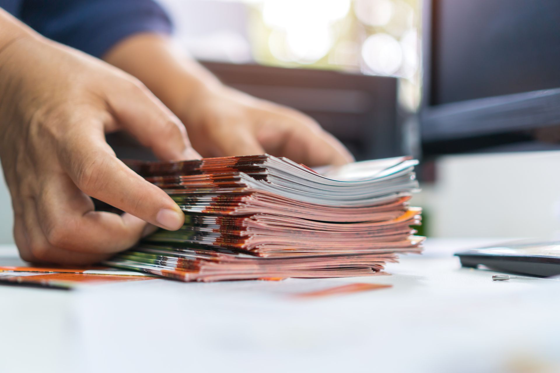 Hands organize a stack of freshly printed marketing cards on a worktable. Hands organize a stack of freshly printed marketing cards on a worktable.
