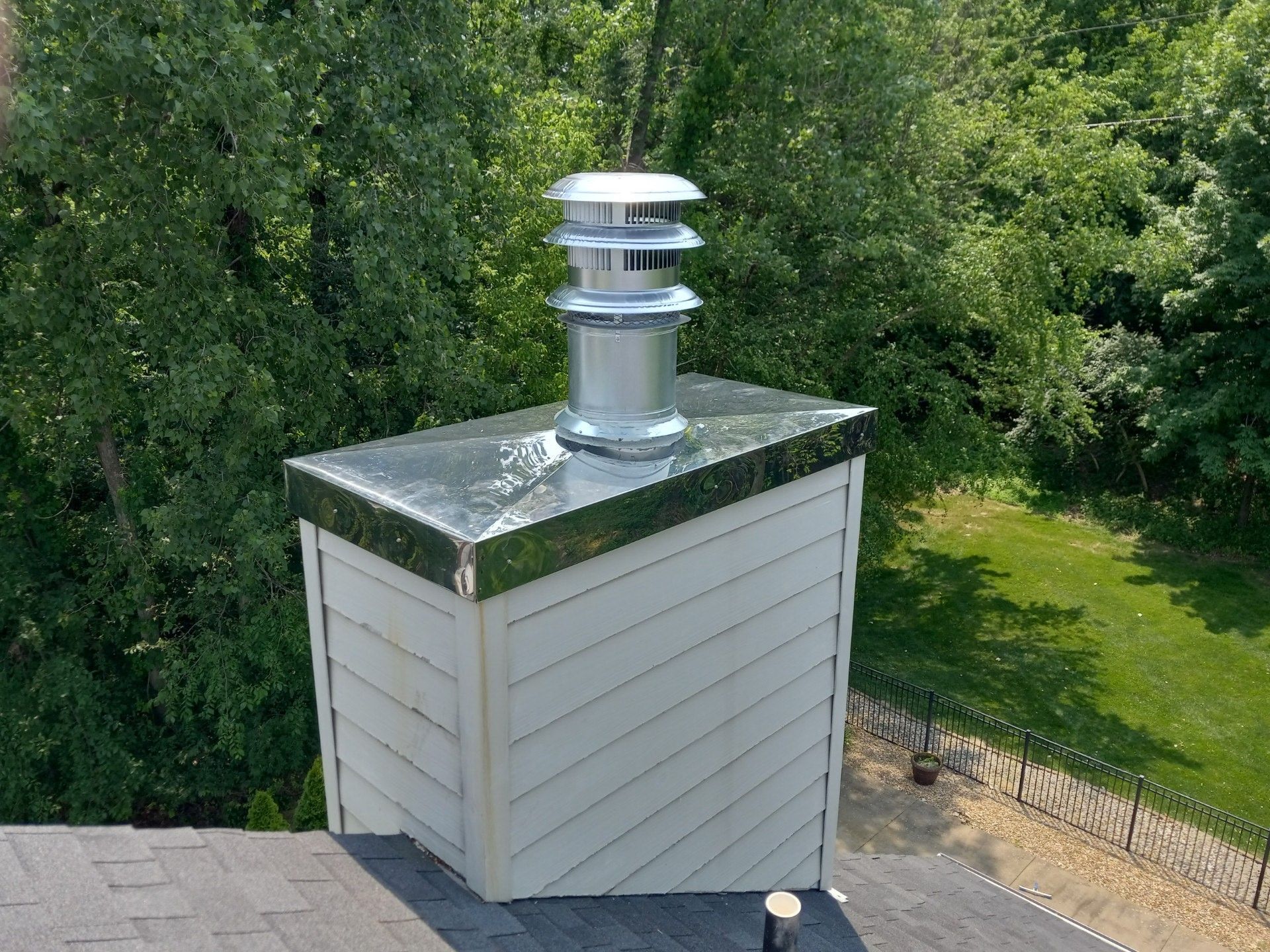 White rooftop vent chimney on a small shed, surrounded by green trees and grass