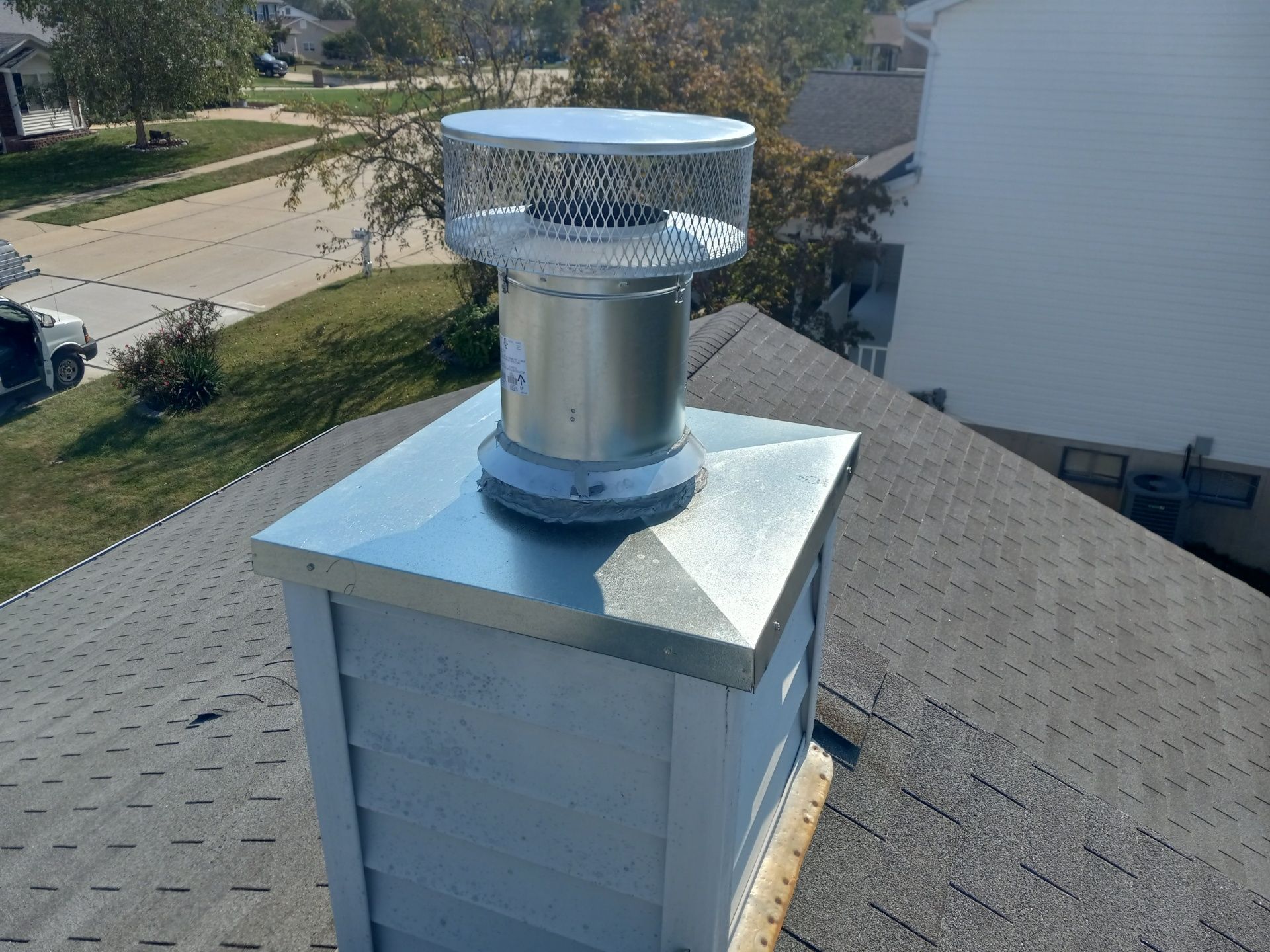 Silver roof vent on a shingled rooftop in a suburban neighborhood