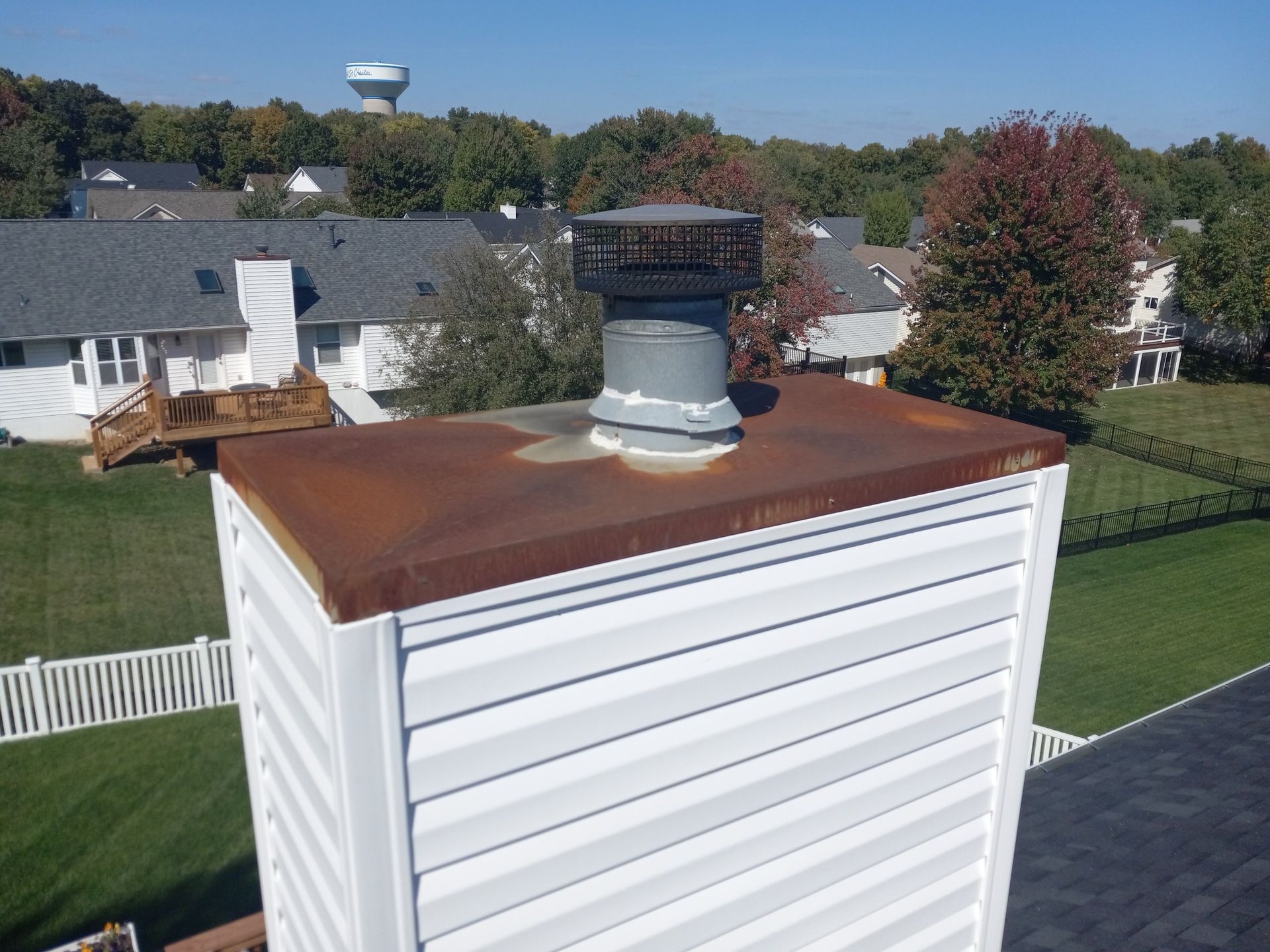 White rooftop vent on a rusted metal roof above suburban houses and trees