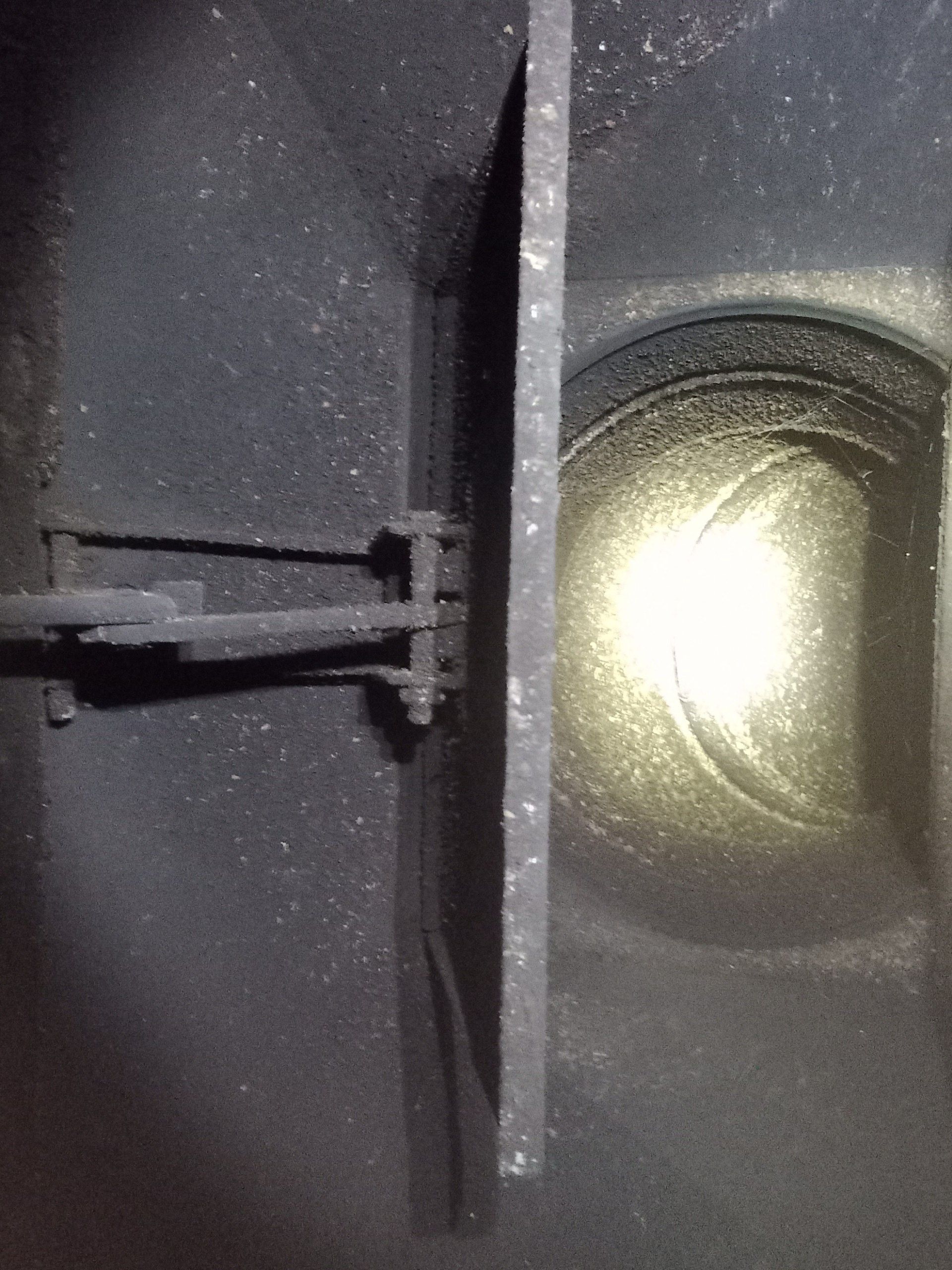 Close-up of a black metal hinge and latch beside a bright circular light inside a dark enclosure
