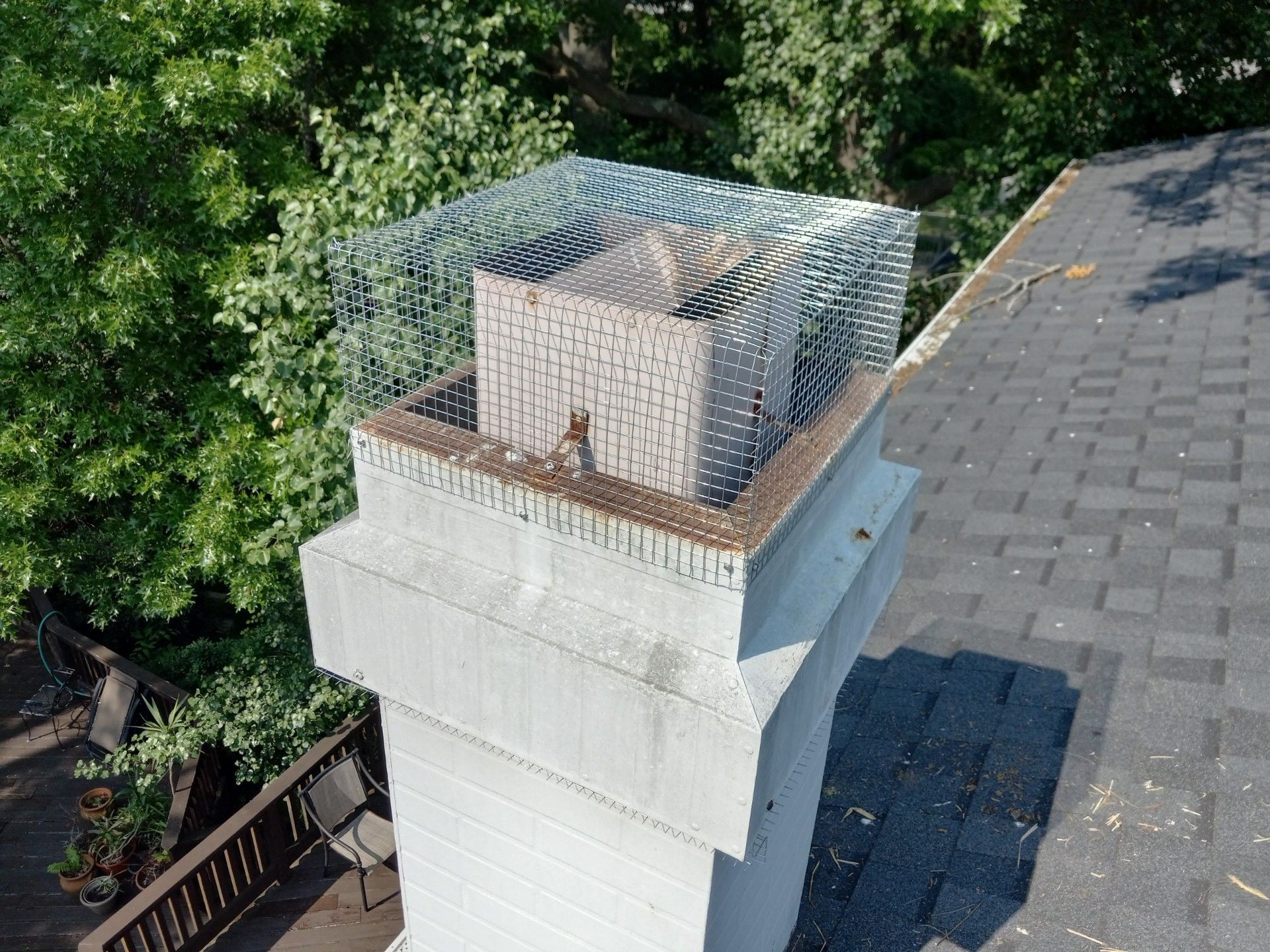 Birdcage-like wire enclosure atop a white rooftop chimney beside a paved roof and trees