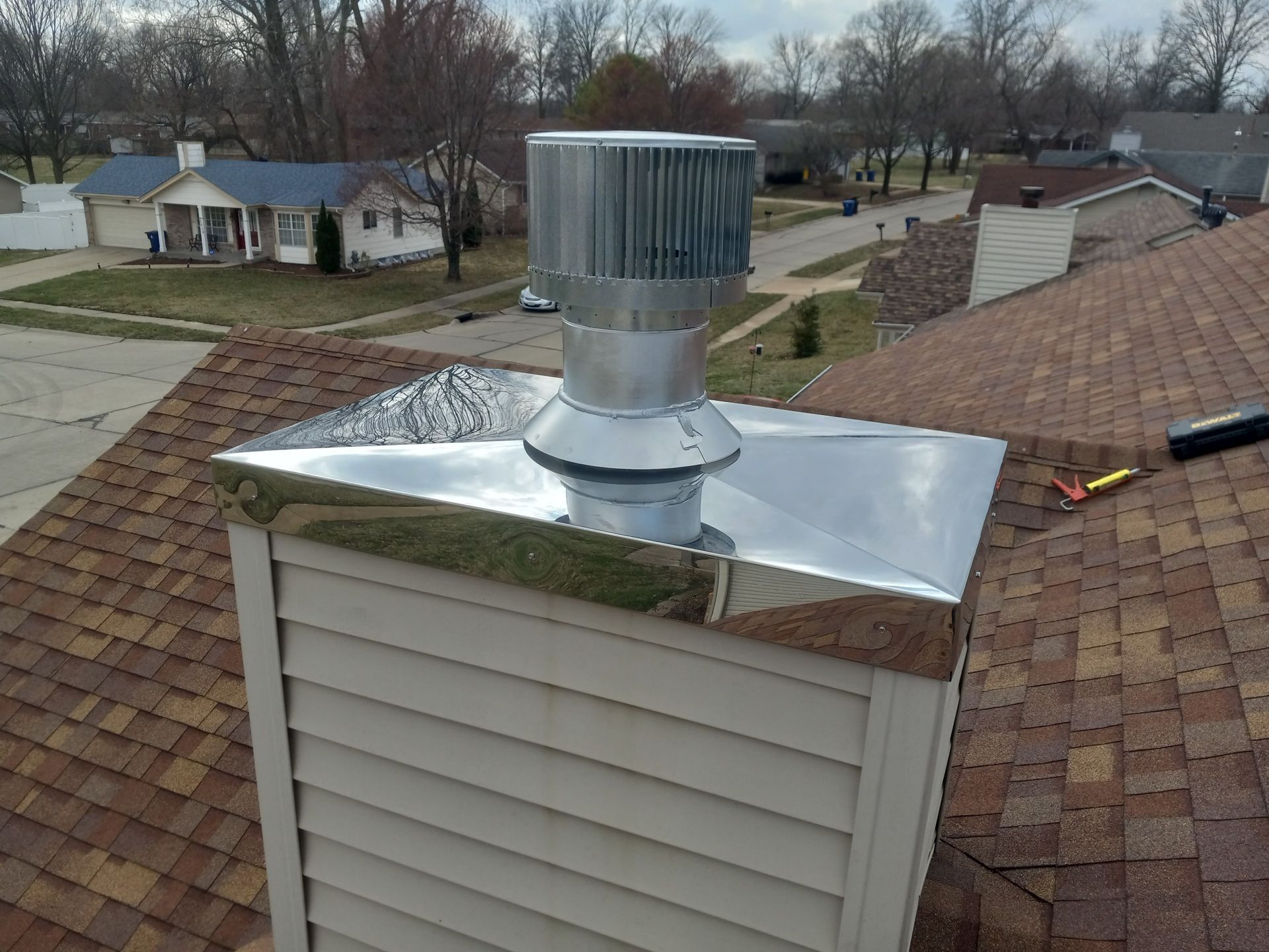 Rooftop vent on a shingled house with shiny metal flashing and a neighborhood visible in the background