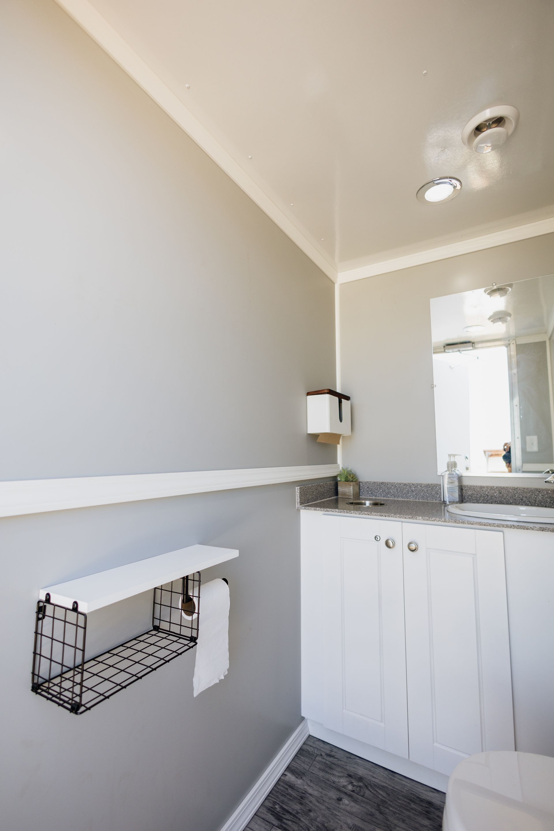 Small bathroom with gray walls, white vanity, mirror, shelf, and wall-mounted toilet paper holder