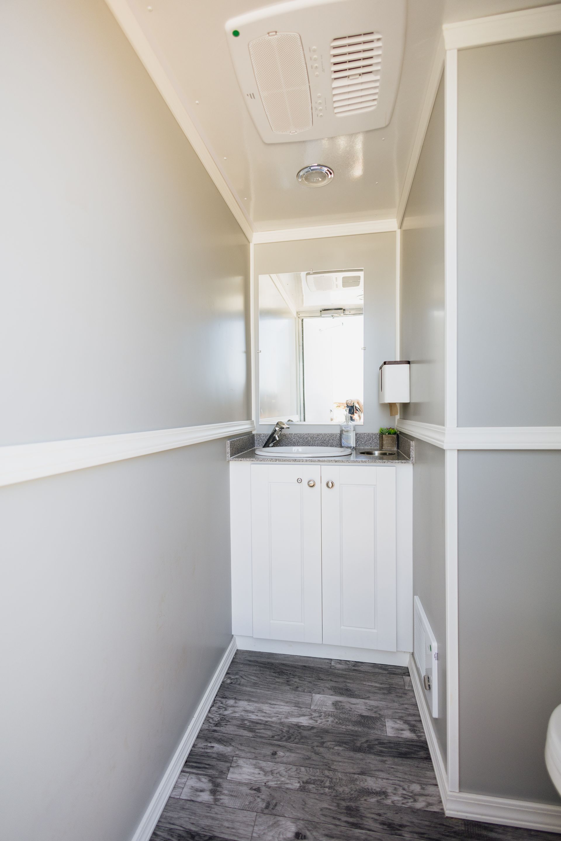 Narrow bathroom vanity with mirror, white cabinets, gray walls, and patterned floor rug