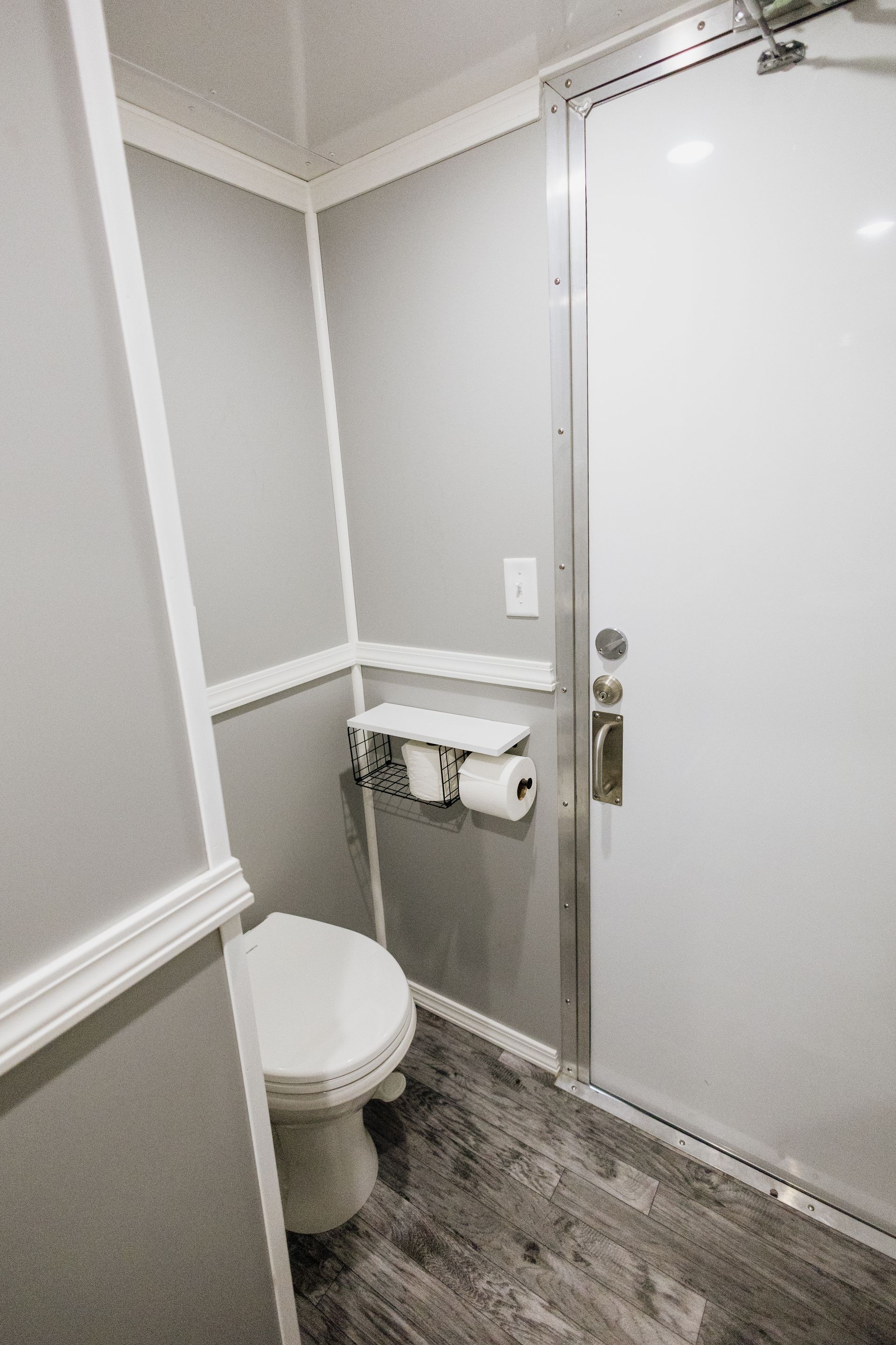 Small bathroom with toilet, wall-mounted paper holder, and closed white door on gray walls.