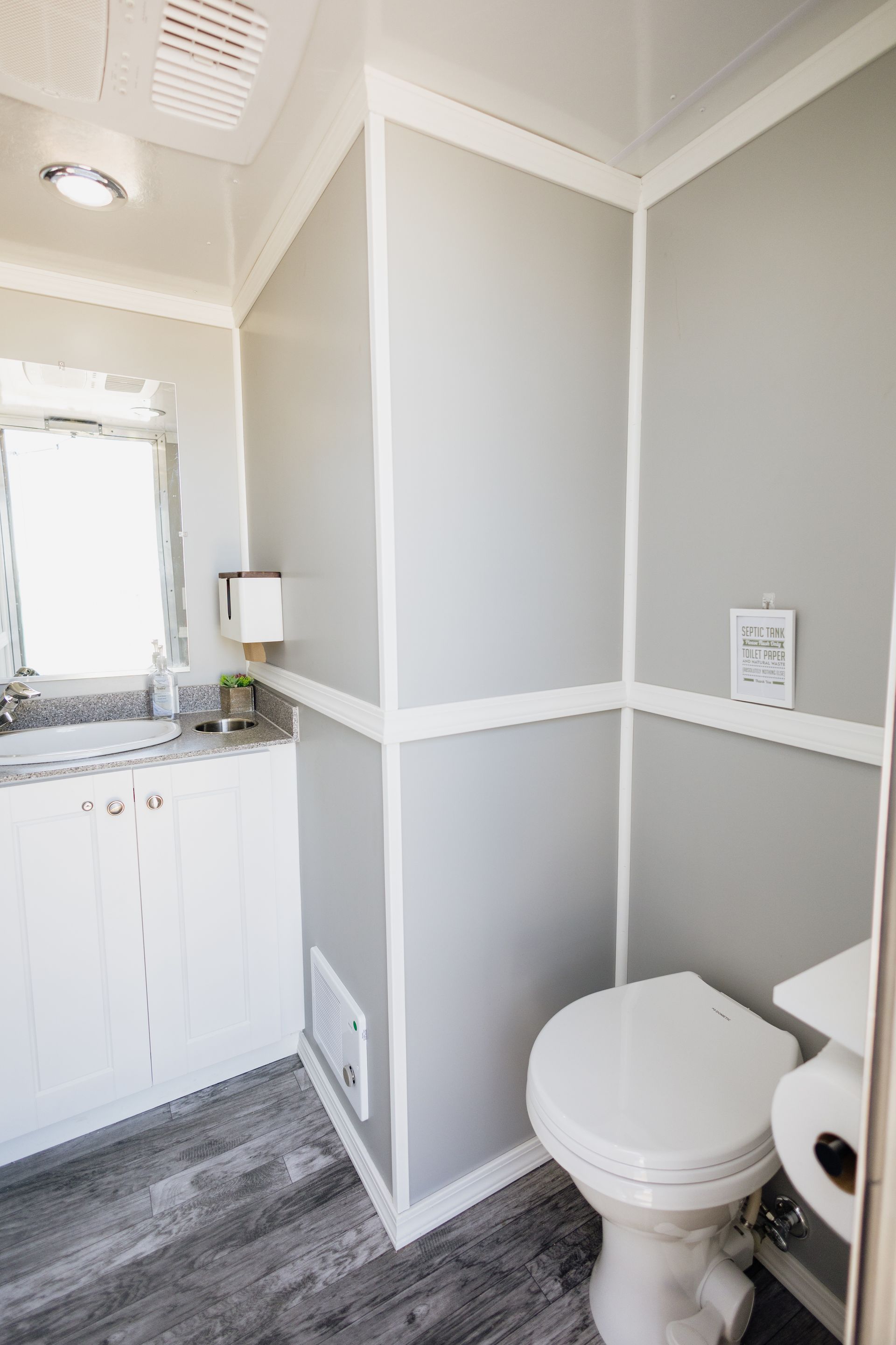 Small gray-and-white bathroom with a toilet, sink vanity, and mirror