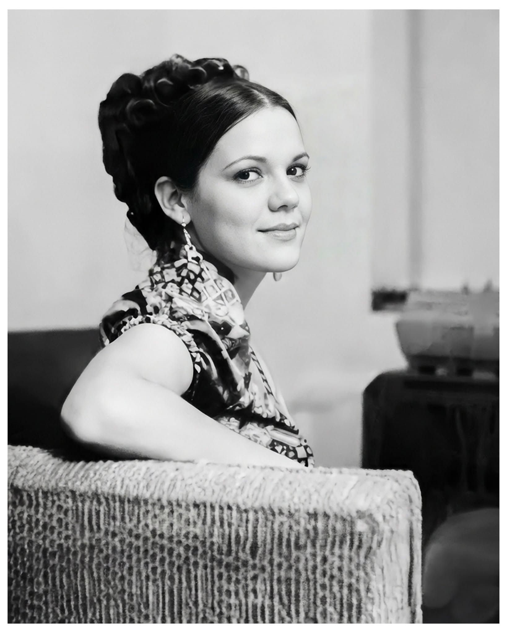 Woman seated on a sofa, looking over her shoulder in a black-and-white portrait