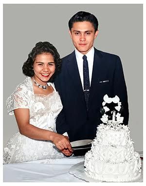 Wedding couple cutting a white tiered cake, the bride smiling in a white dress beside the groom in a dark suit.