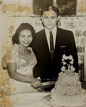 Couple posing beside a decorated cake at a celebration, smiling in formal attire.