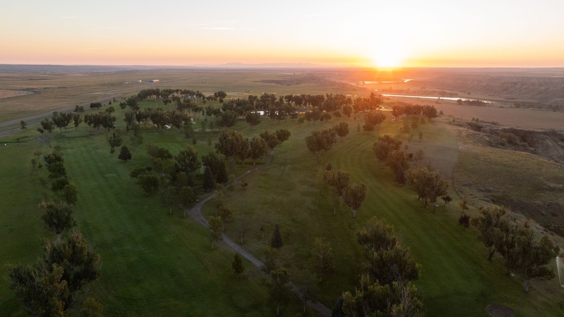 Aerial view of a golf course landscape during a golden sunrise with trees scattered across rolling green hills.