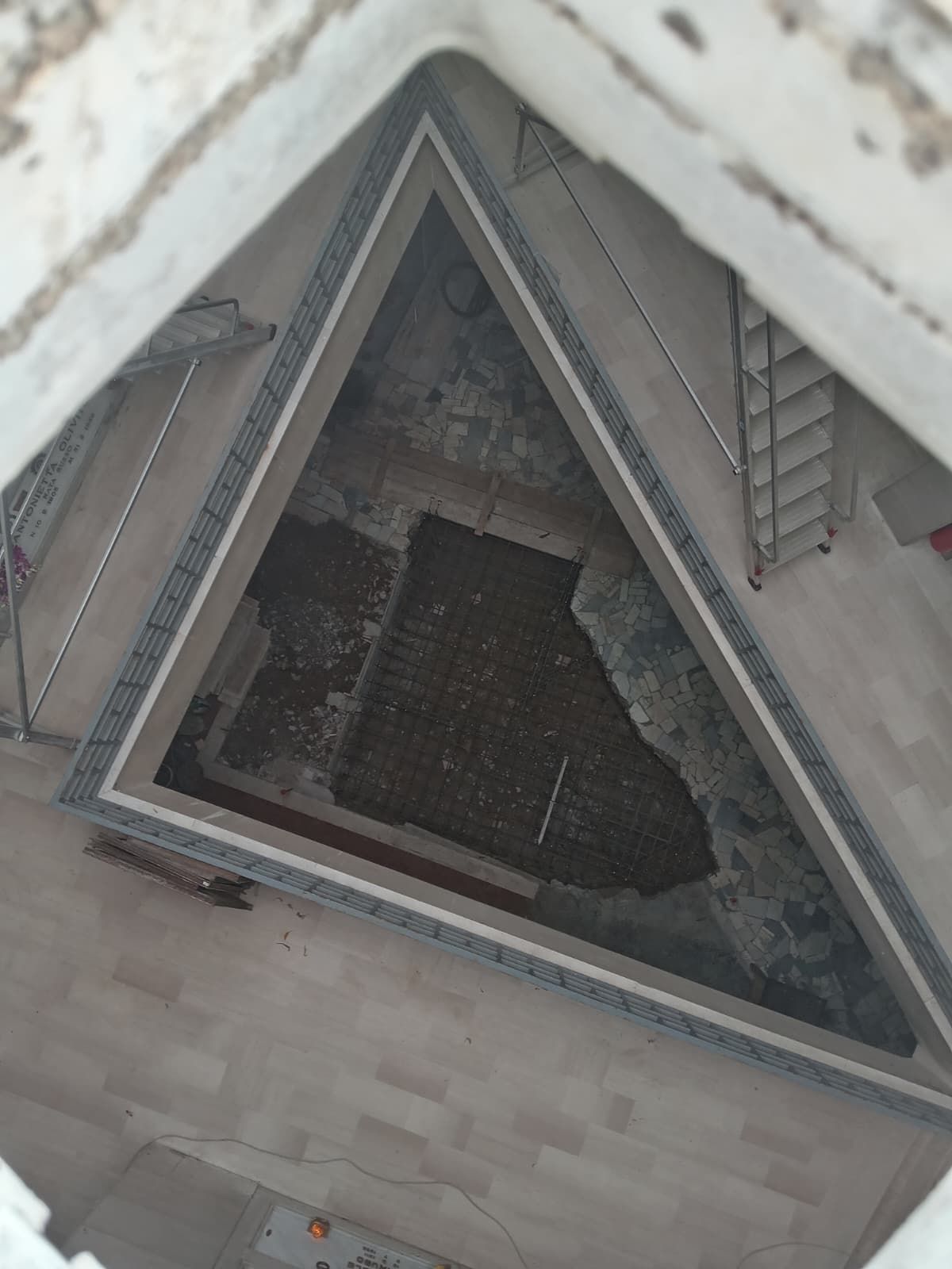 Veduta aerea di un cortile triangolare con pavimentazione in pietra, una zona centrale scura e scalinate su entrambi i lati.