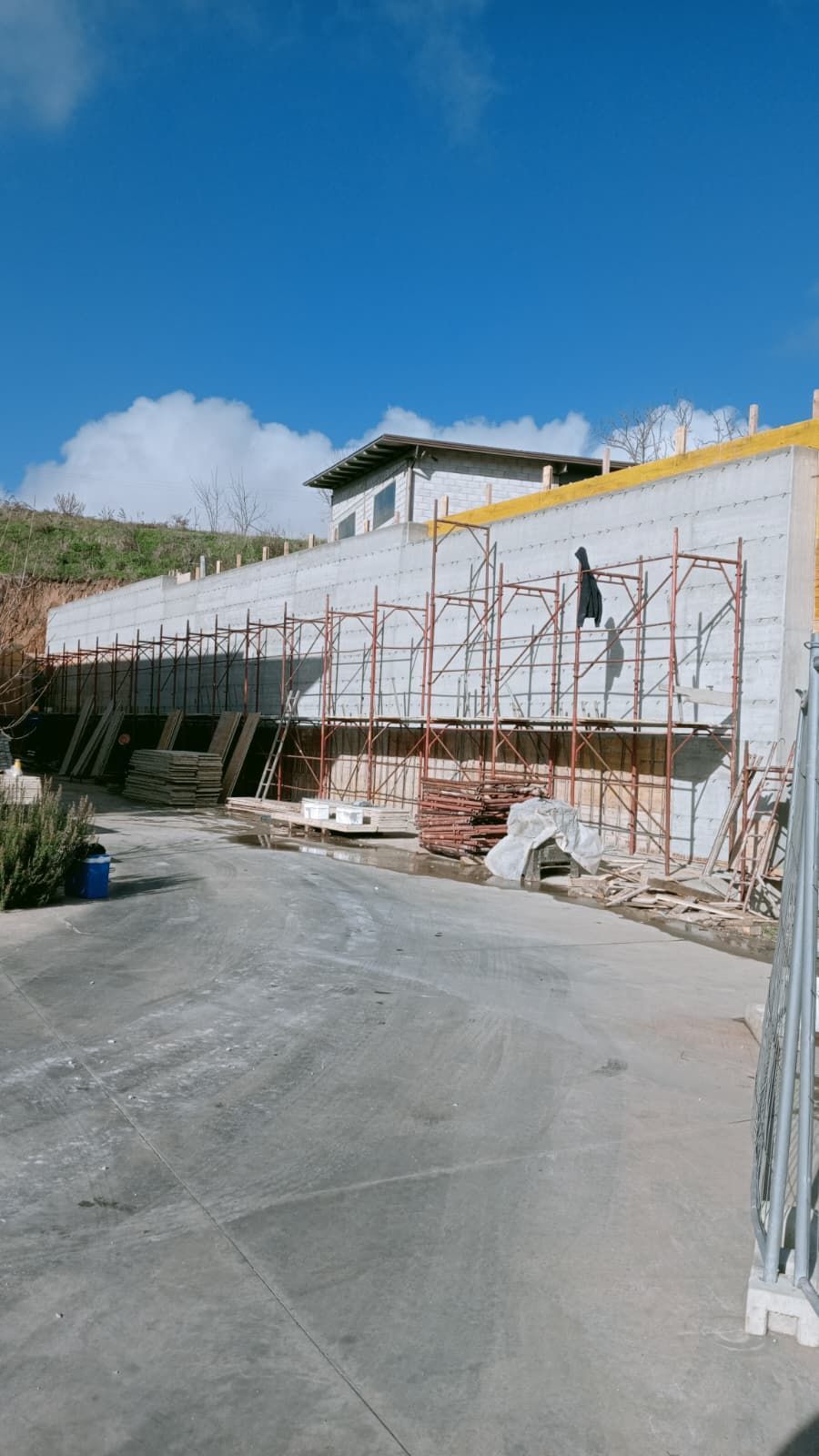 Impalcature lungo un muro bianco in un cantiere edile sotto un cielo azzurro brillante.
