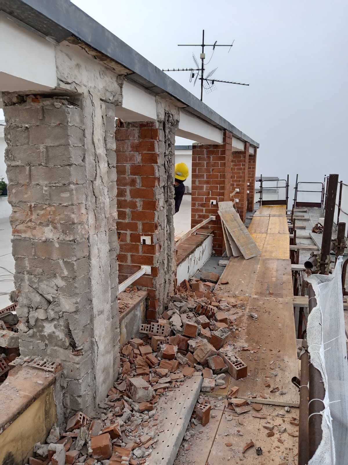 Edificio in mattoni parzialmente demolito con macerie sul pavimento e un operaio con una maglietta gialla sullo sfondo.