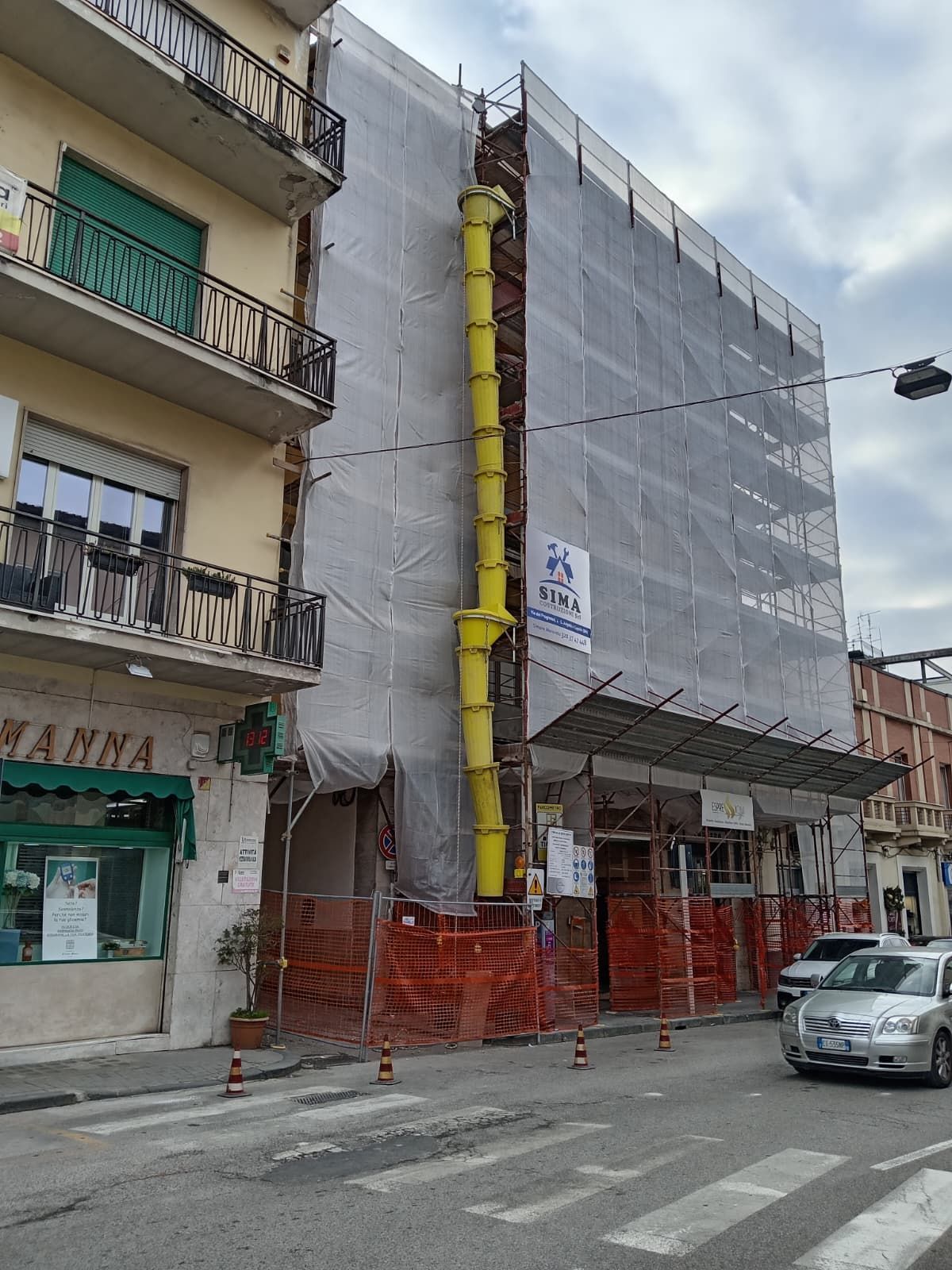 Vista stradale di un edificio in fase di ristrutturazione, avvolto da impalcature e reti protettive grigie.