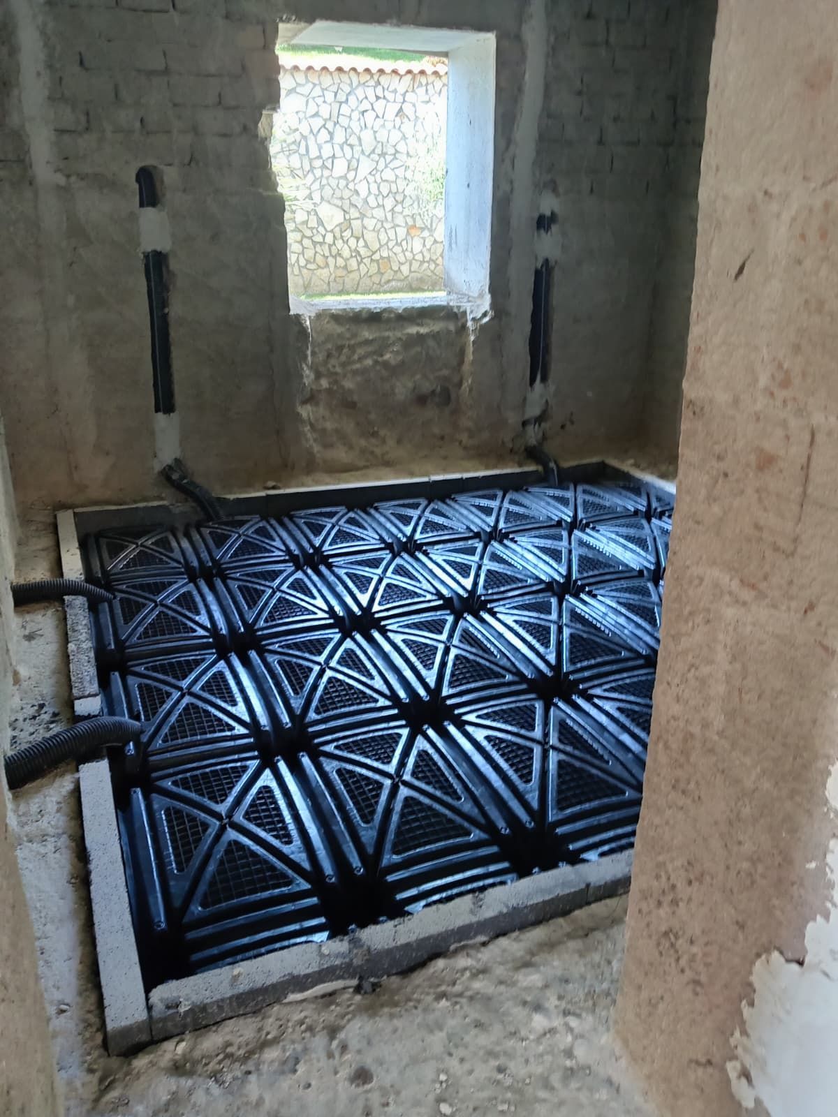 Piccolo bagno non rifinito con pavimento in piastrelle geometriche nere e una finestra che lascia entrare la luce.
