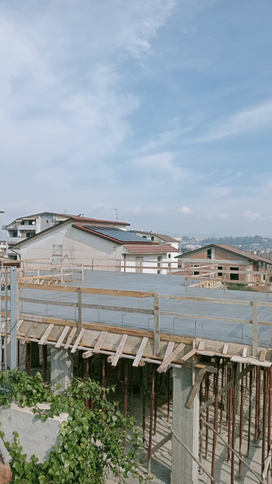 Cantiere edile sul tetto con impalcature di legno, un telone blu e case sotto un cielo nuvoloso.