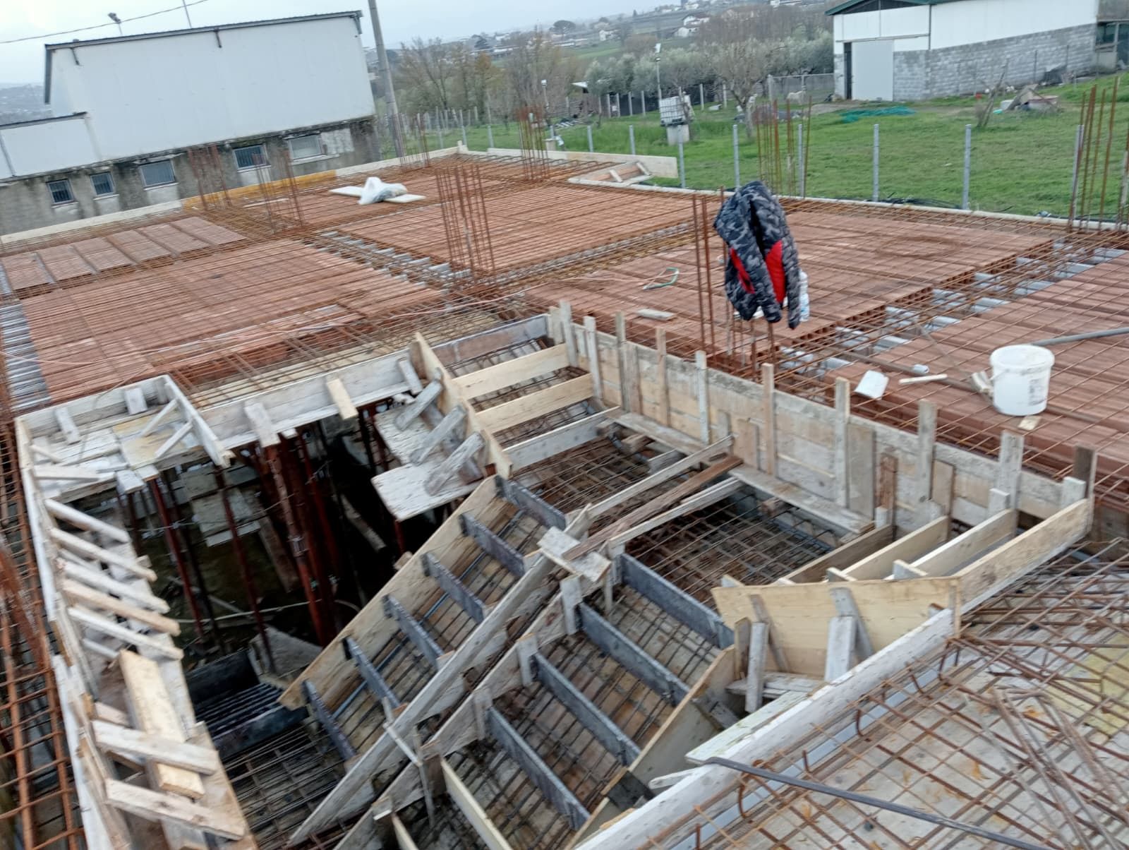 Cantiere edile con una grande fossa di cemento, casseforme in legno e barre d'armatura arrugginite in cima.