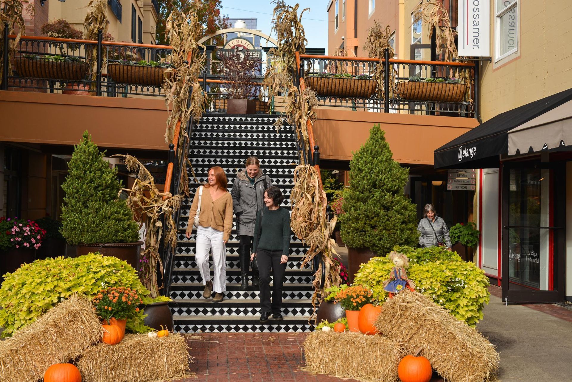 Three people walk down the black-and-white tiled staircase at the 5th Street Public Market in Eugene, Oregon, surrounded by fall décor including pumpkins, hay bales, cornstalks, and autumn greenery. The Market’s cozy, festive atmosphere reflects the neighborhood charm just steps from Gordon Lofts — where dining, shopping, and local events come together in the heart of downtown Eugene.