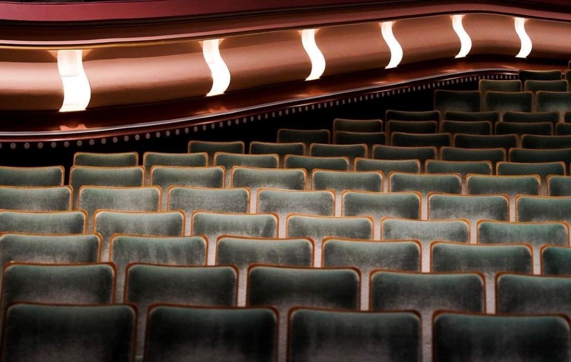 A view of the elegant interior seating at the Hult Center. Rows of plush green chairs with golden trim are illuminated by soft, curved wall lights, creating a warm and inviting ambiance in the iconic performance venue.