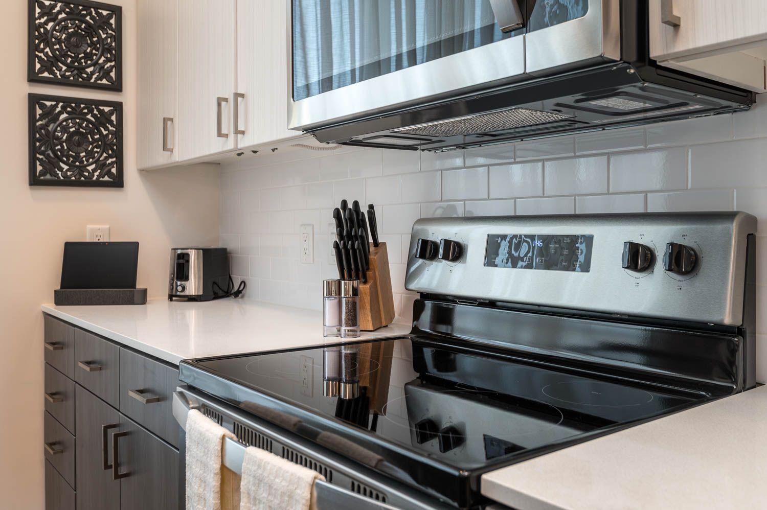 A modern kitchen space featuring a stainless steel electric stove and microwave, white backsplash, sleek dark cabinets, and a neatly arranged countertop with a knife block, salt and pepper shakers, and a toaster.
