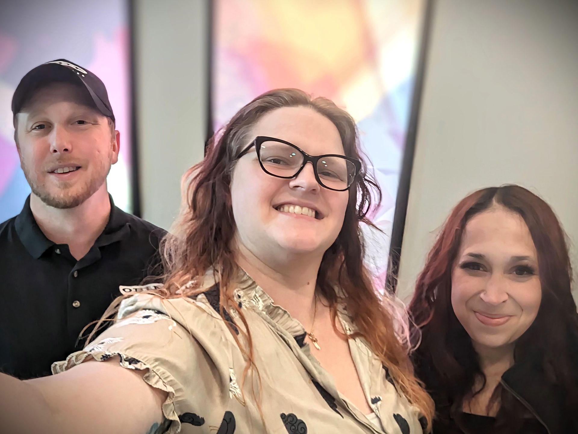 A cheerful group photo of Gordon Lofts team members. Three individuals stand together, smiling warmly at the camera, with a colorful abstract background adding a vibrant and welcoming touch.