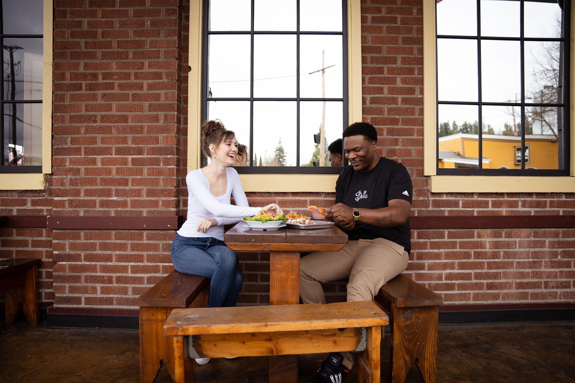 A couple relaxing on an outdoor patio bench enjoying lunch, smiling and laughing