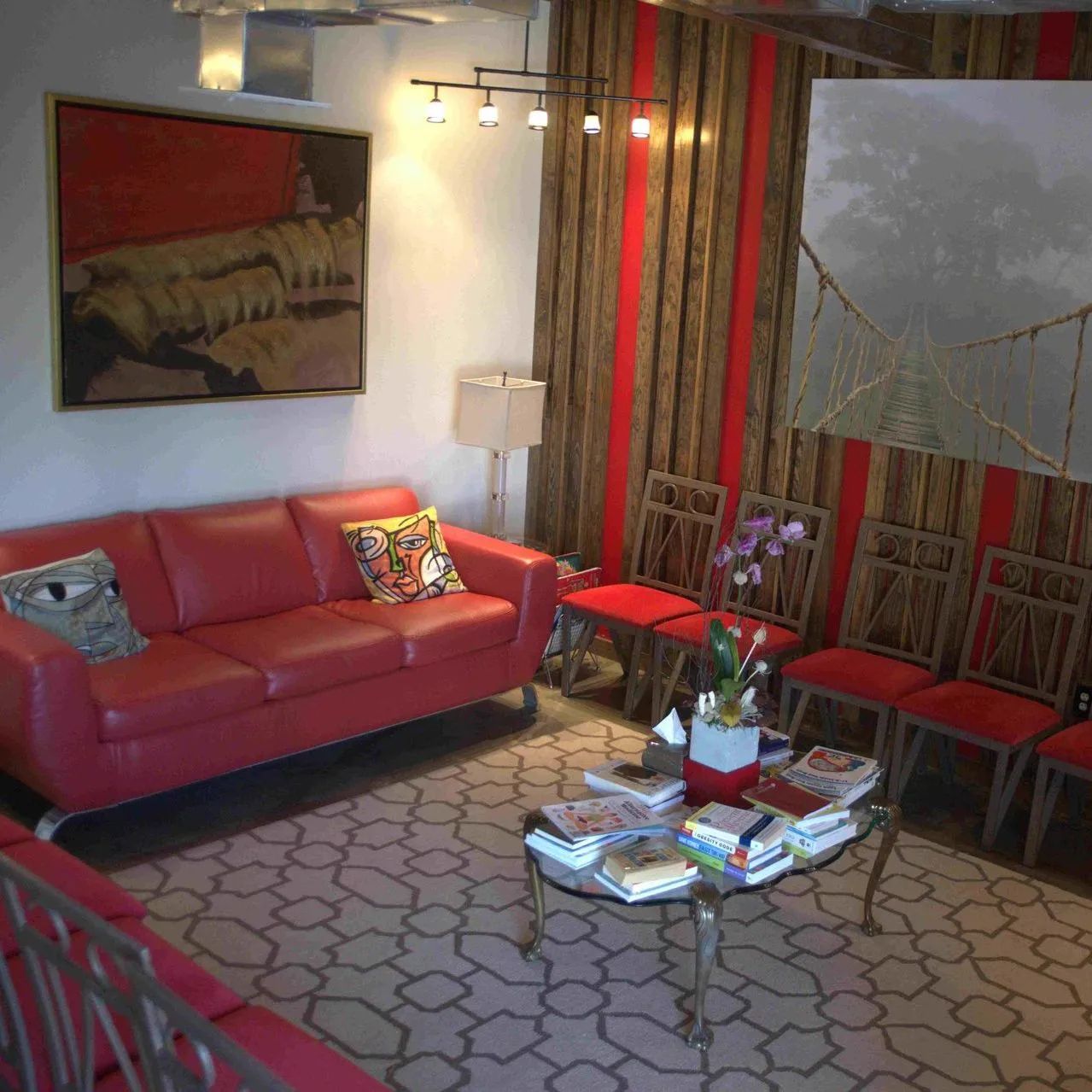 A waiting room with red sofa and chairs, coffee table with books, art, and wooden wall panels.