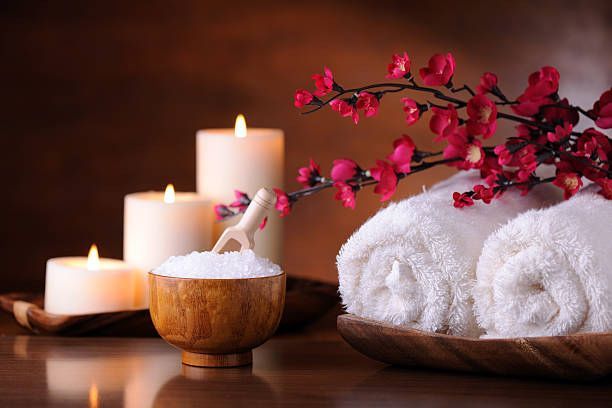 Spa setting: white towels, lit candles, salt in bowl, red flowers.