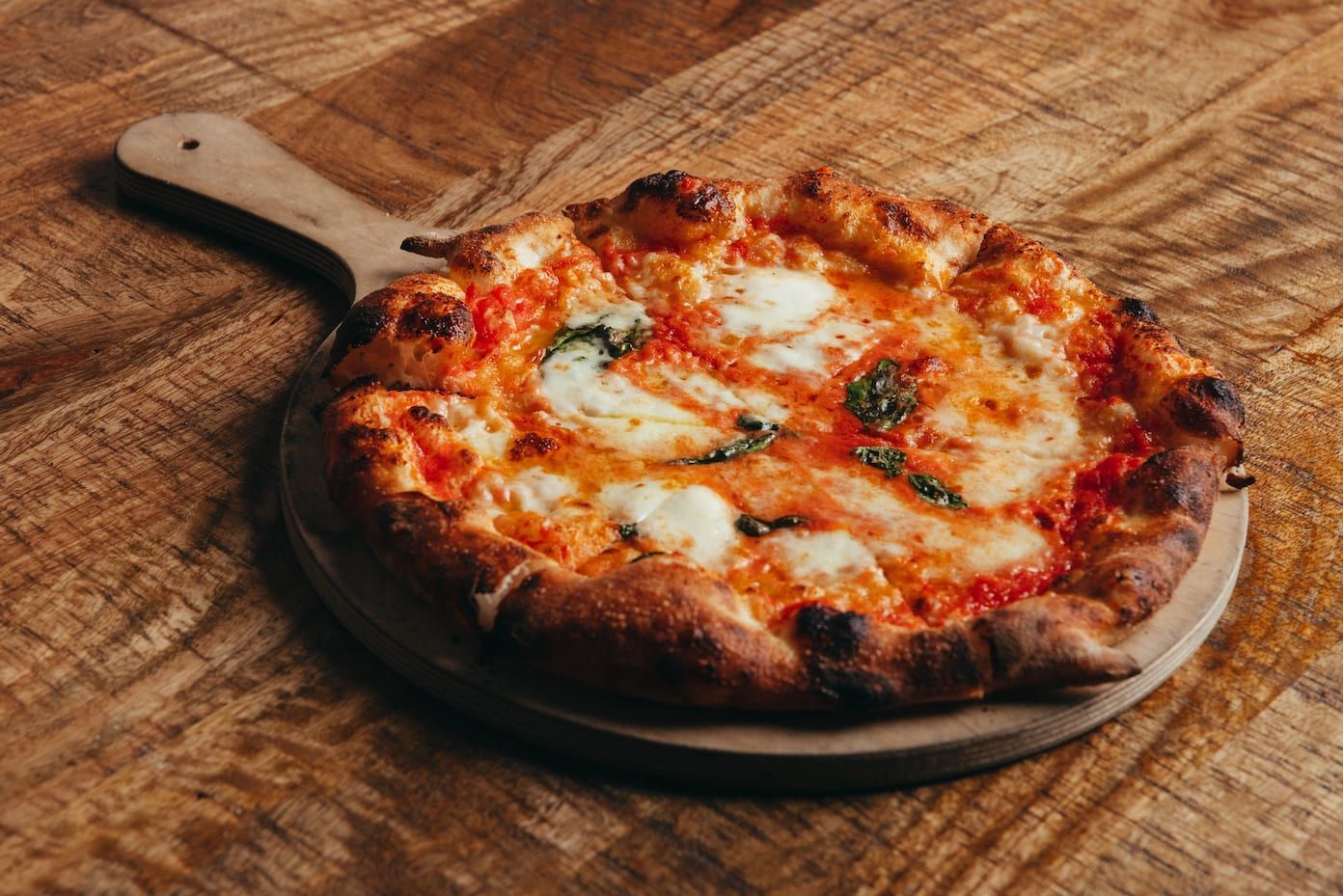 A pizza is sitting on a wooden cutting board on a wooden table.