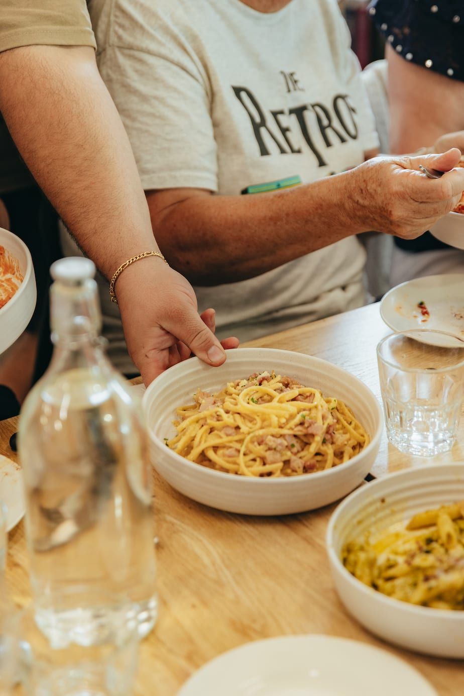 Person serving a bowl of pasta from a table filled with dishes of food.