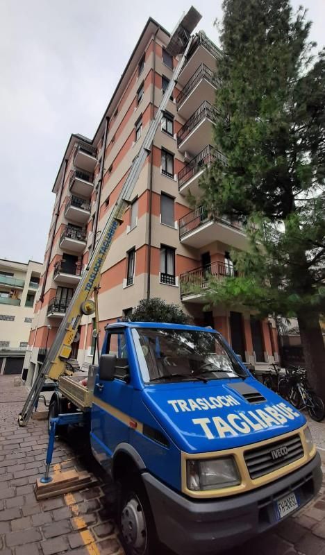 Carro attrezzi blu parcheggiato accanto a un alto edificio residenziale, con una scala estesa lungo la facciata.