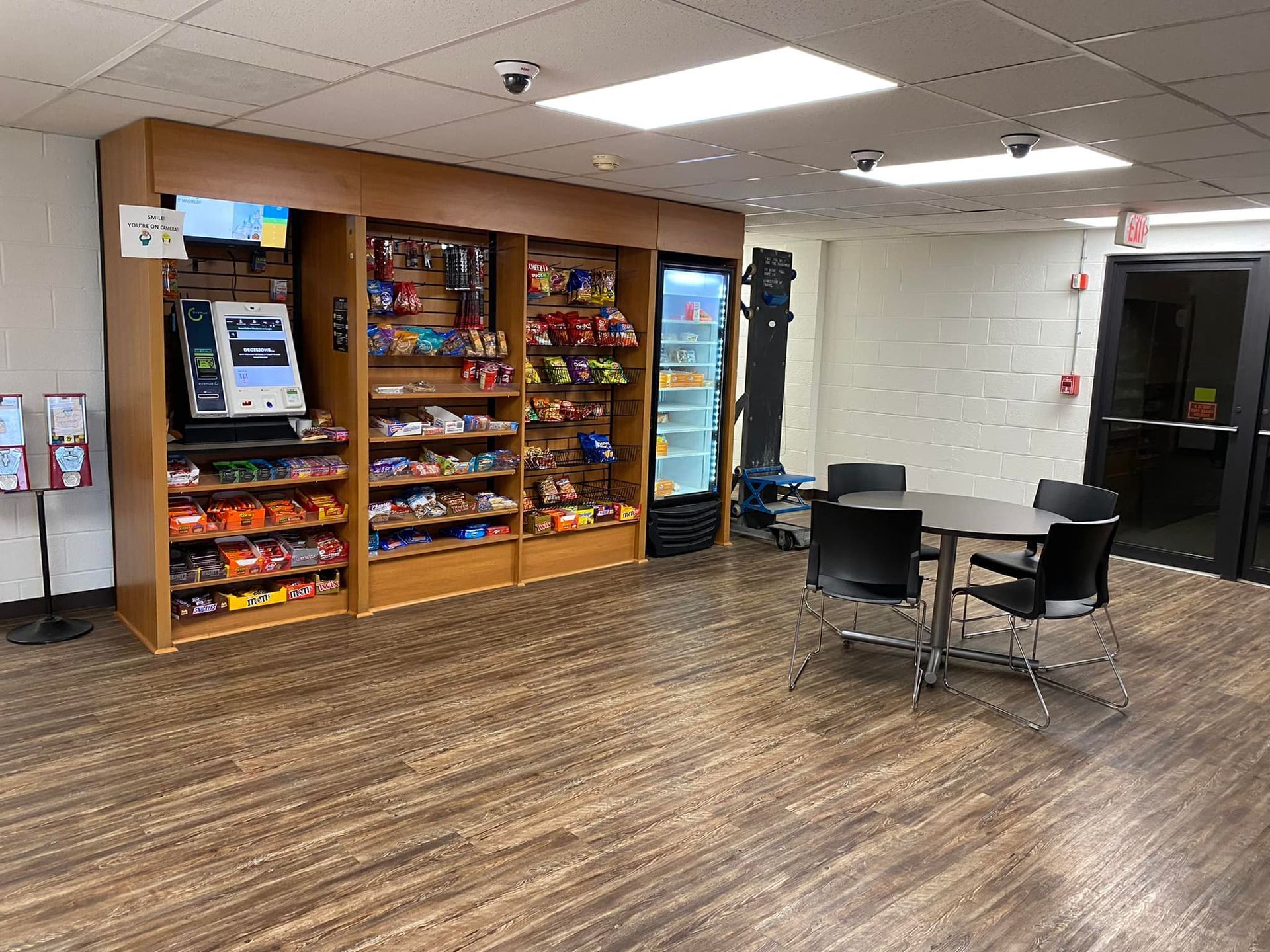 A room with a table , chairs , shelves and a vending machine.