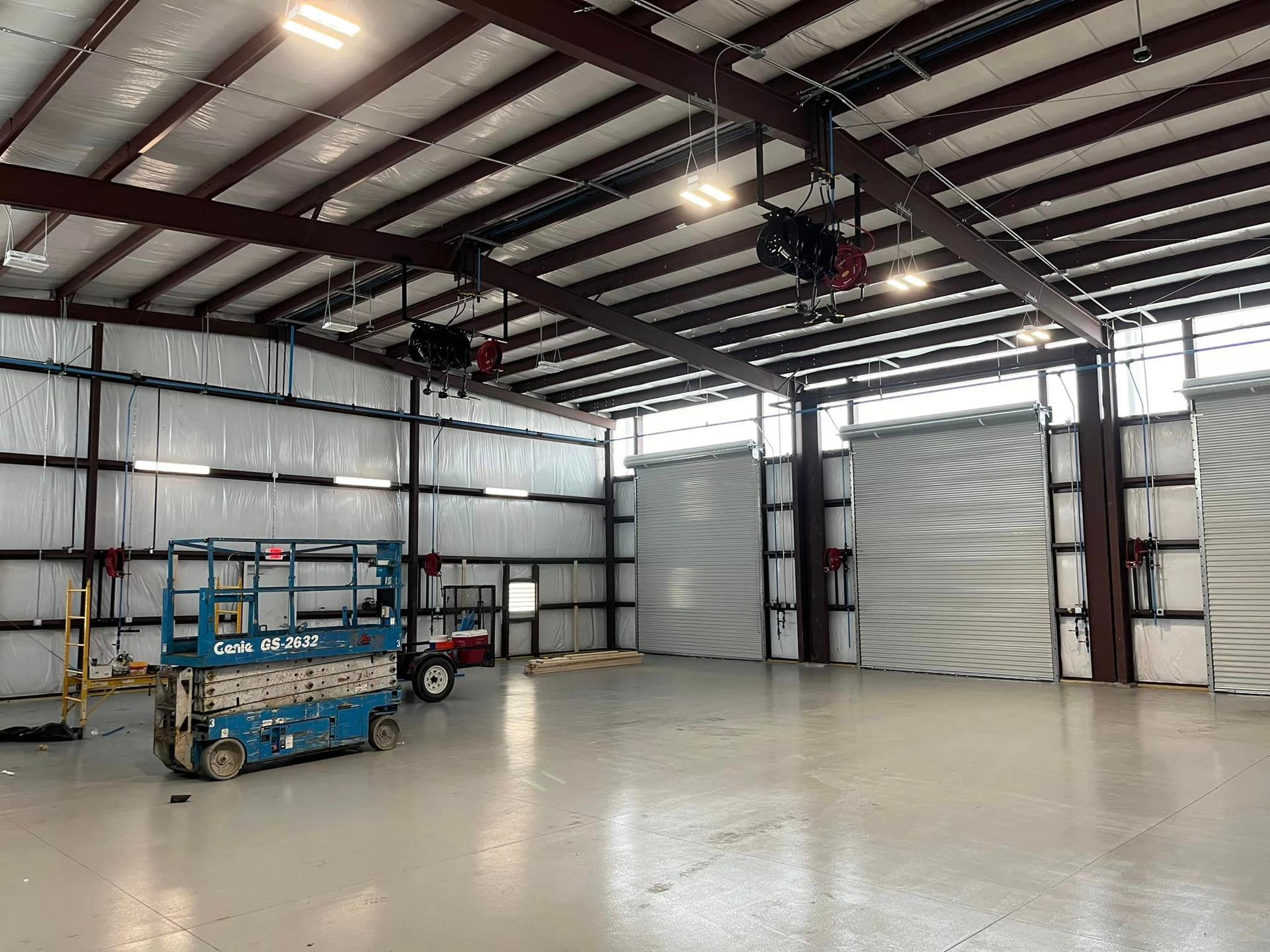 A blue scissor lift is parked inside of a large warehouse.