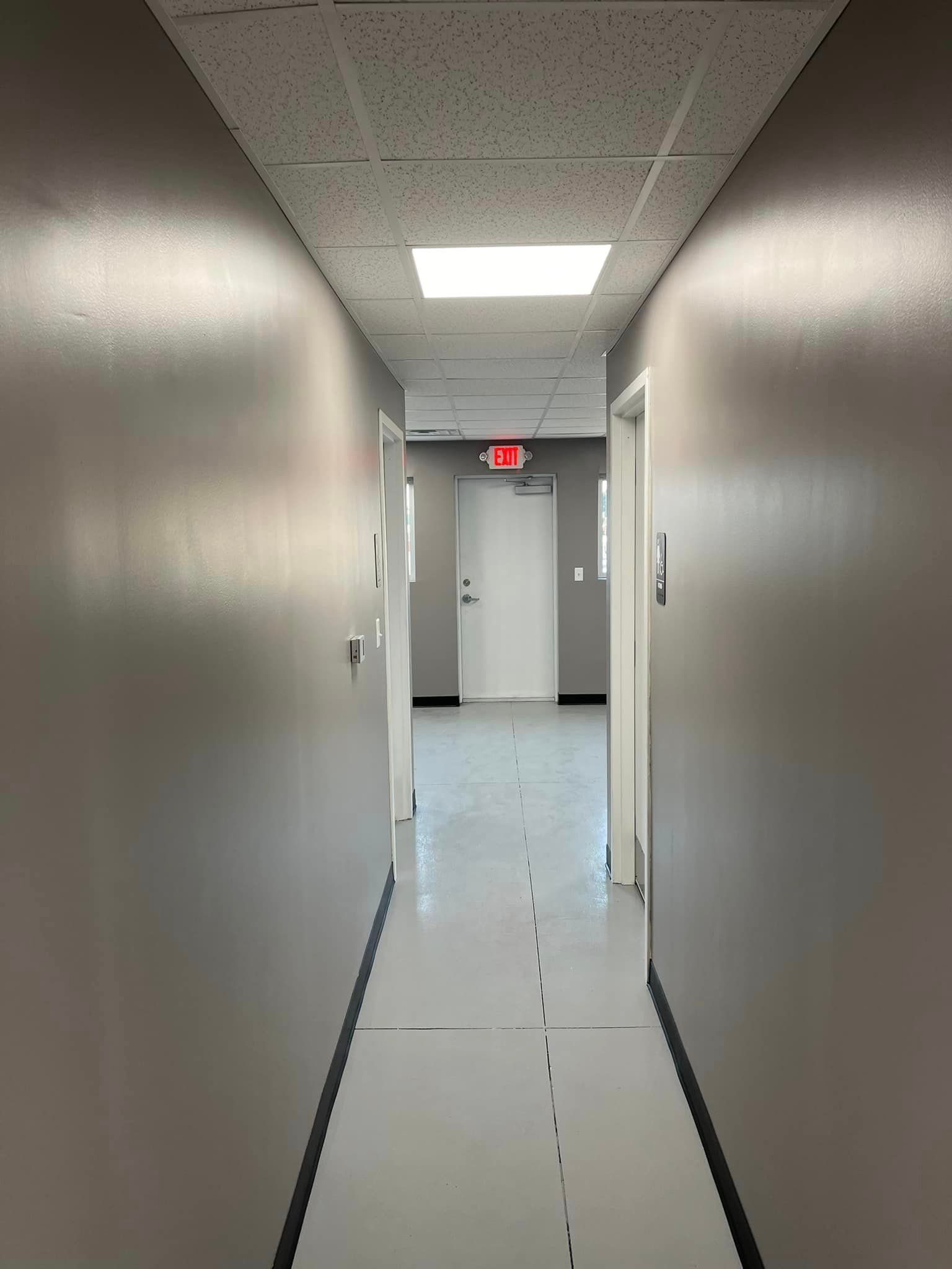 A long hallway with a red exit sign on the ceiling.