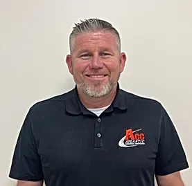 A man with a beard is wearing a black polo shirt and smiling.