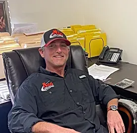 A man wearing a hat is sitting in a chair in front of a desk.