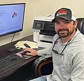 A man is sitting at a desk in front of a computer and printer.