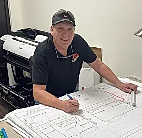 A man is sitting at a desk looking at a blueprint.