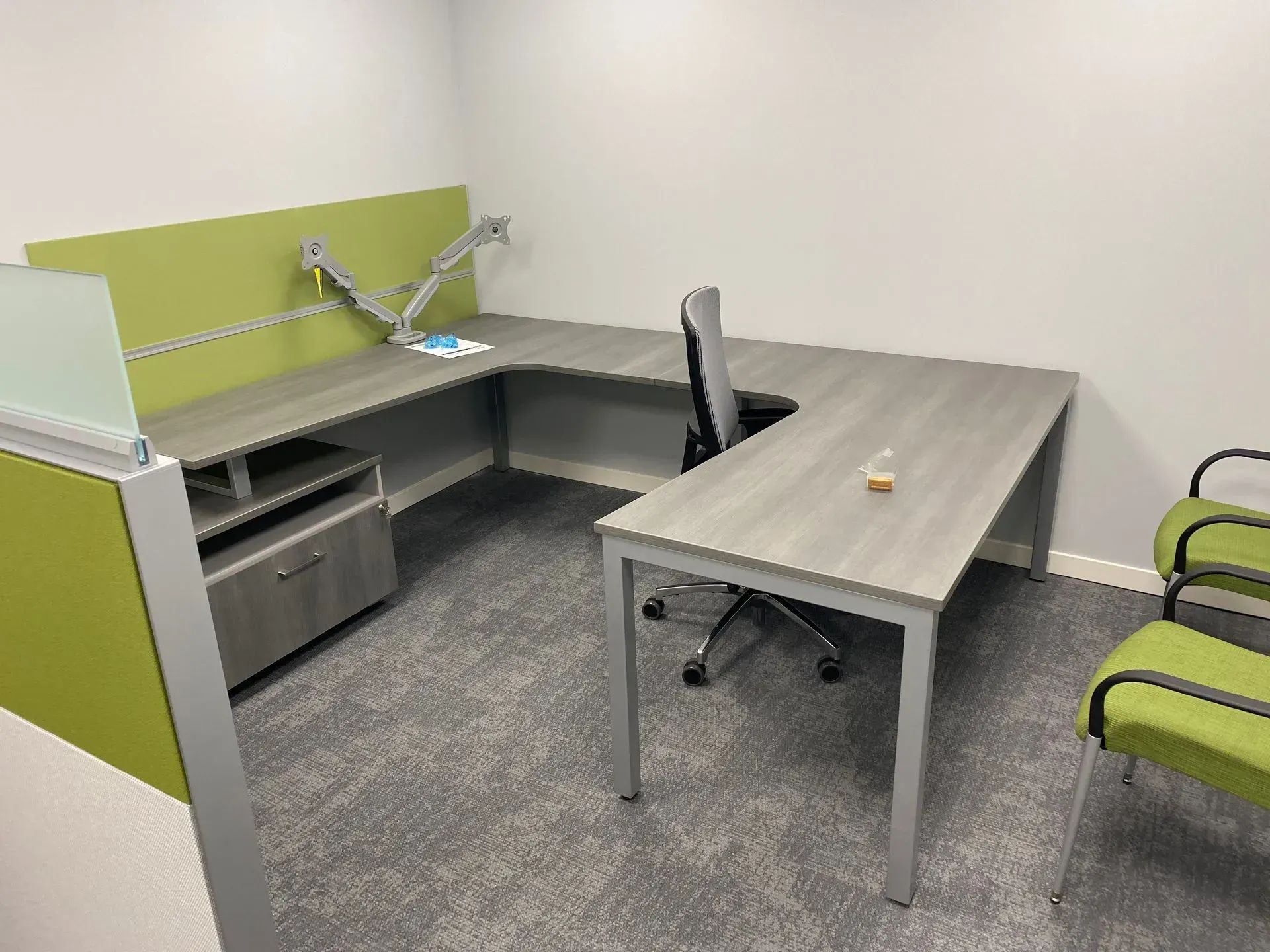 Open office workspace with cubicles, fluorescent lighting, and blue carpet. A person stands near the entrance.
