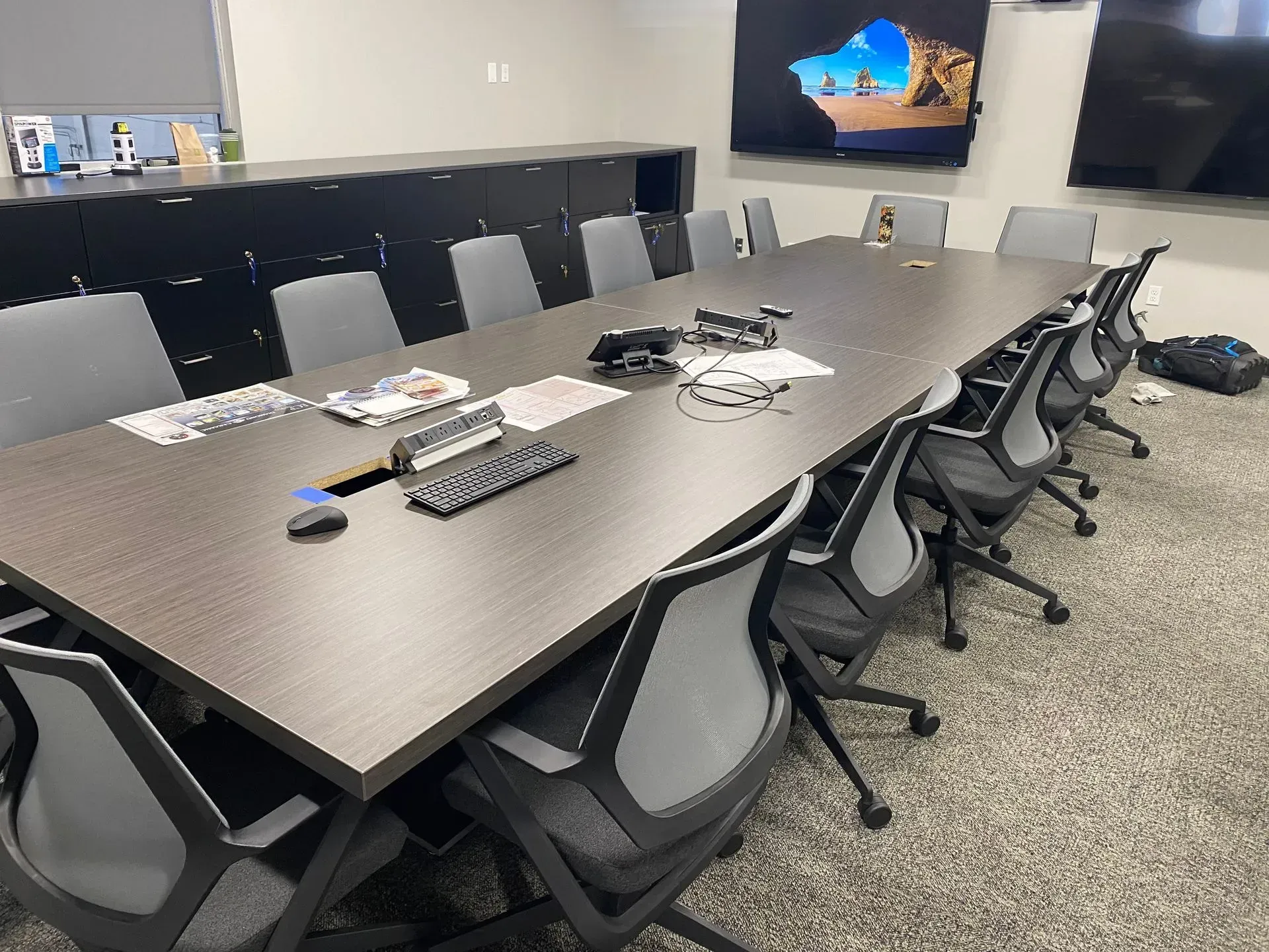 A conference room with a long table, chairs, and a couple of screens on the wall.