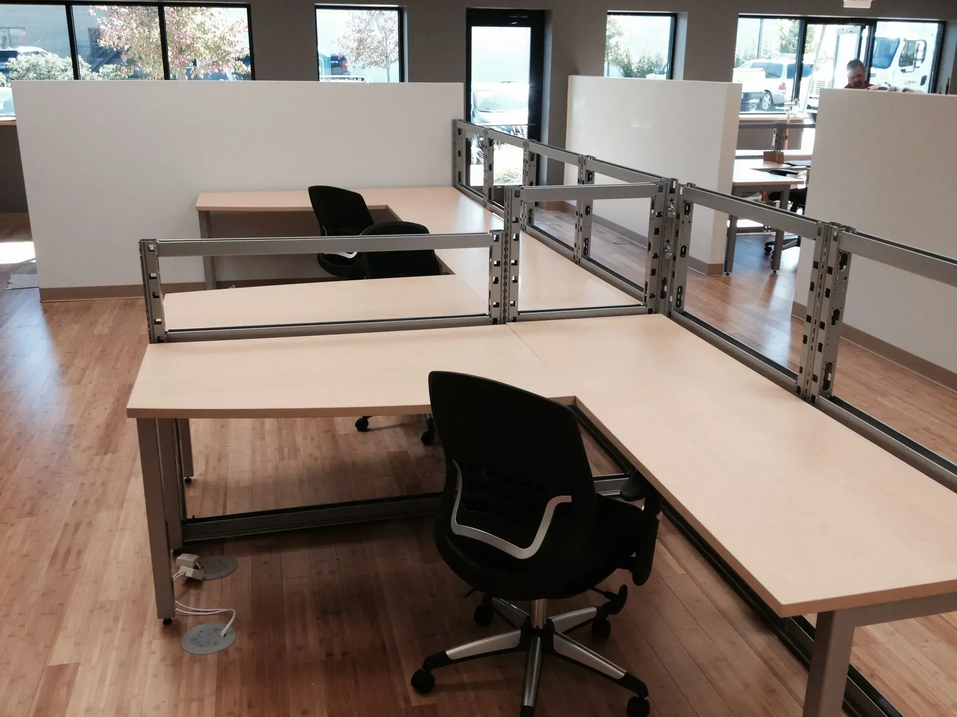 L-shaped office desks with black chairs, separated by metal frames.