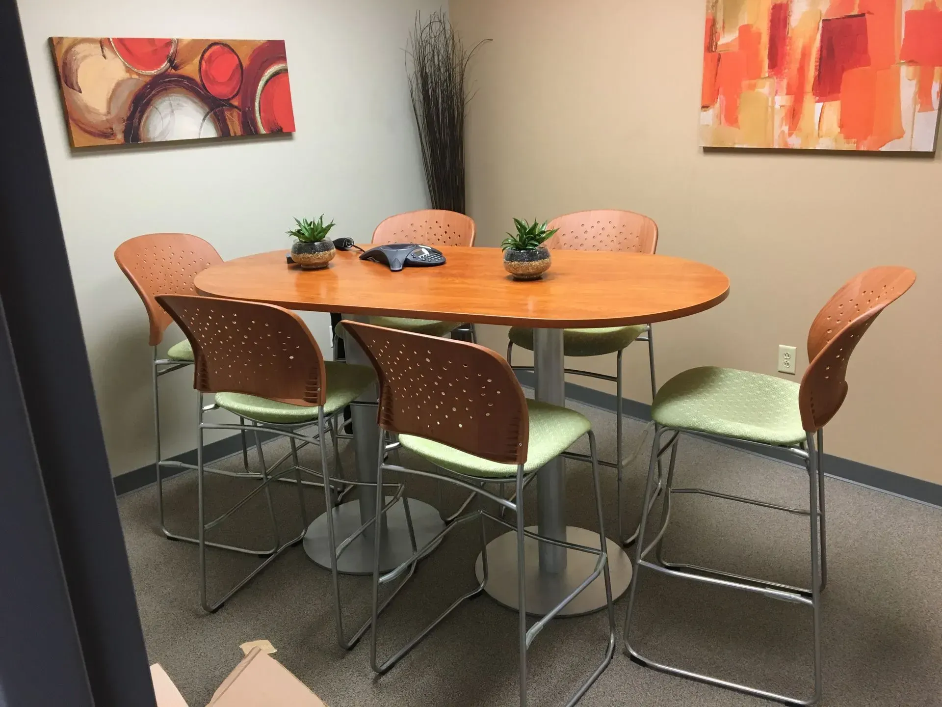 Orange lounge chairs in a modern office waiting area, lit by tall lamps. A large window shows trees outside.