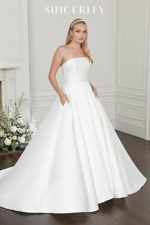 A woman in a white wedding dress is standing in front of a fireplace.
