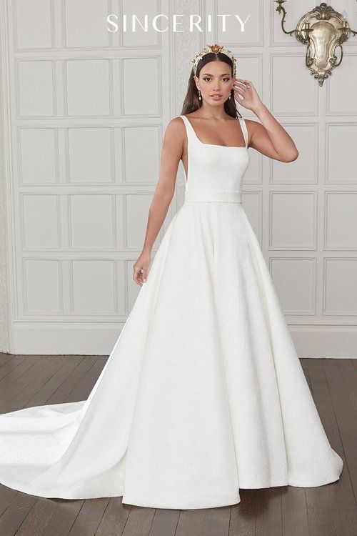 A woman in a white wedding dress is standing in front of a wall.