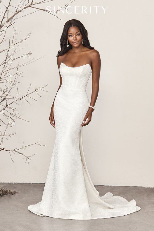 A woman in a white wedding dress is standing in front of a tree.