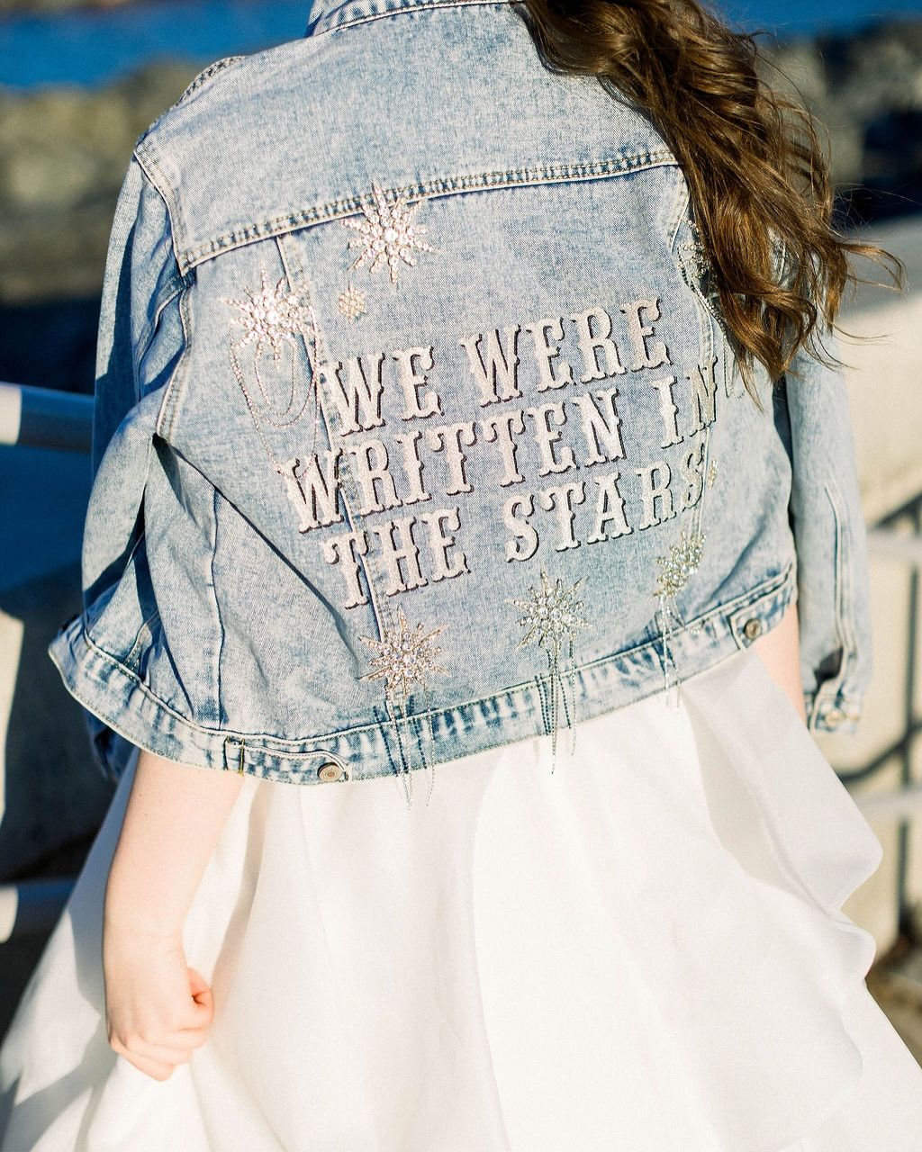 A woman in a white dress wears a denim jacket embroidered with 