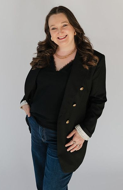 A woman wearing a black shirt and a necklace is smiling in a black and white photo.