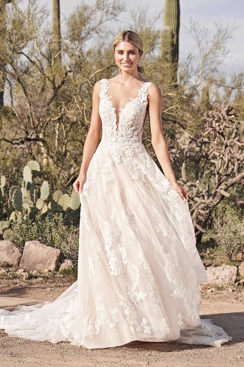 A woman in a wedding dress is standing in front of a cactus.